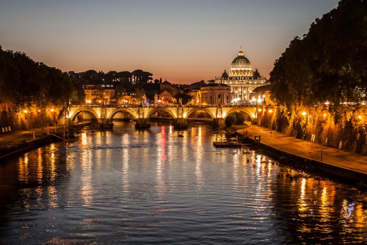 Scenic nighttime view of a bridge and illuminated dome over a river in a city.