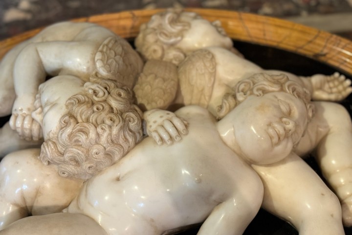 Marble sculpture of sleeping cherubs with wings lying on each other in a circular arrangement.
