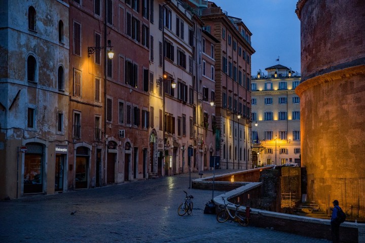 Street in Rome at dusk with lit buildings and bicycles parked along the sidewalk.