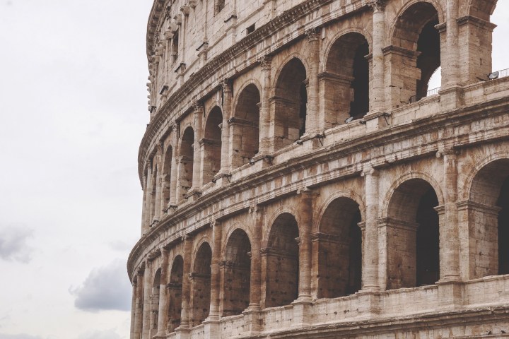 Close-up of the Colosseum's exterior, showing ancient stone arches against a cloudy sky.