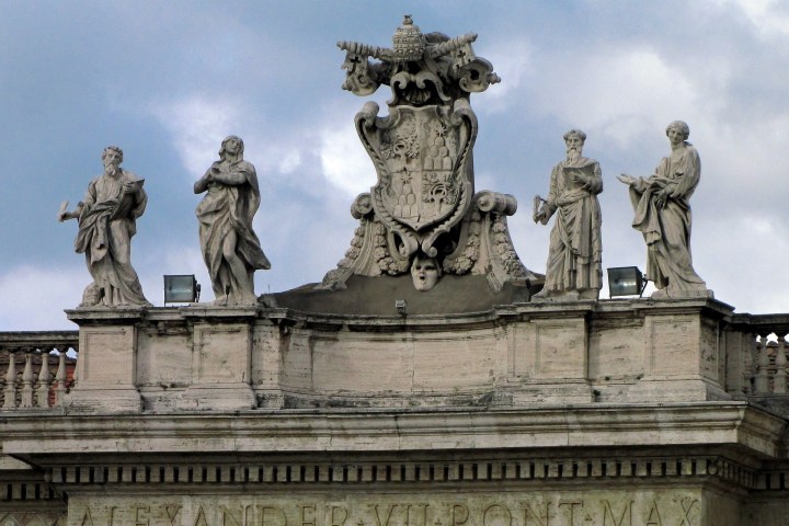 Stone statues and ornate crest atop a building with inscription 'Alexander VII Pont Max.'