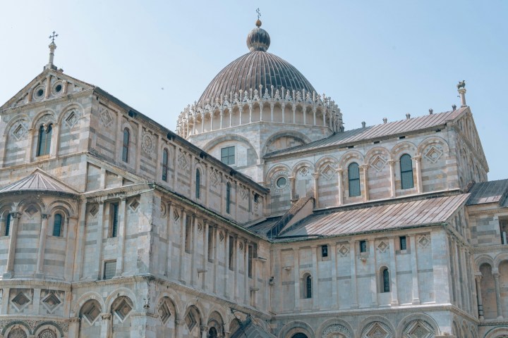 Ornate stone cathedral with arches and domed roof against clear blue sky.
