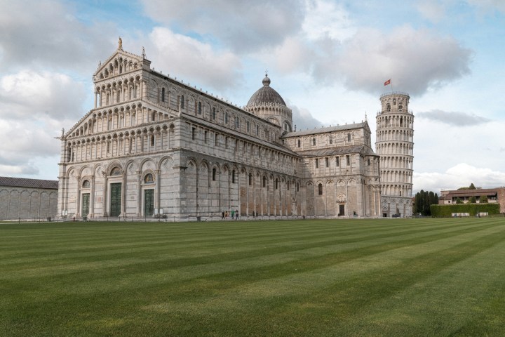 Leaning Tower of Pisa with cathedral and green lawn under cloudy sky.