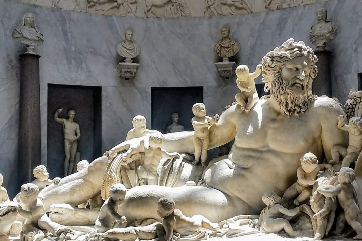 Large marble statue of reclining deity surrounded by multiple small figures in a museum setting.