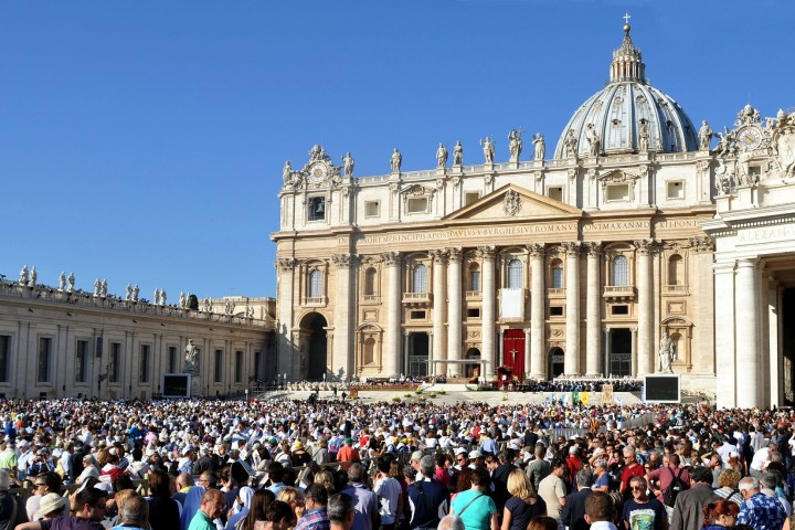 Large crowd gathered in front of St. Peter's Basilica under a clear blue sky.