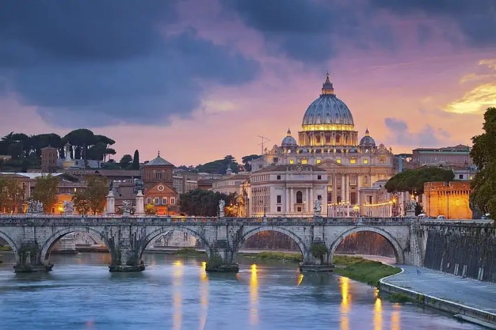 St. Peter's Basilica in Rome at sunset, with a bridge over the Tiber River.