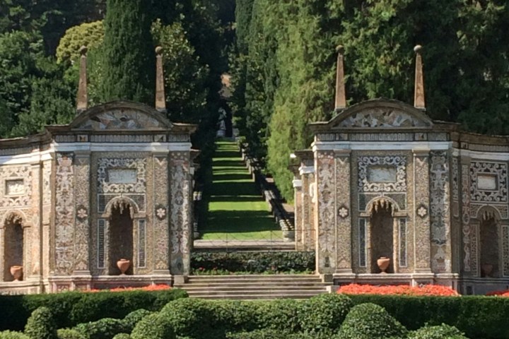Ornate garden with two symmetrical stone arches, lush greenery, and red flower beds.